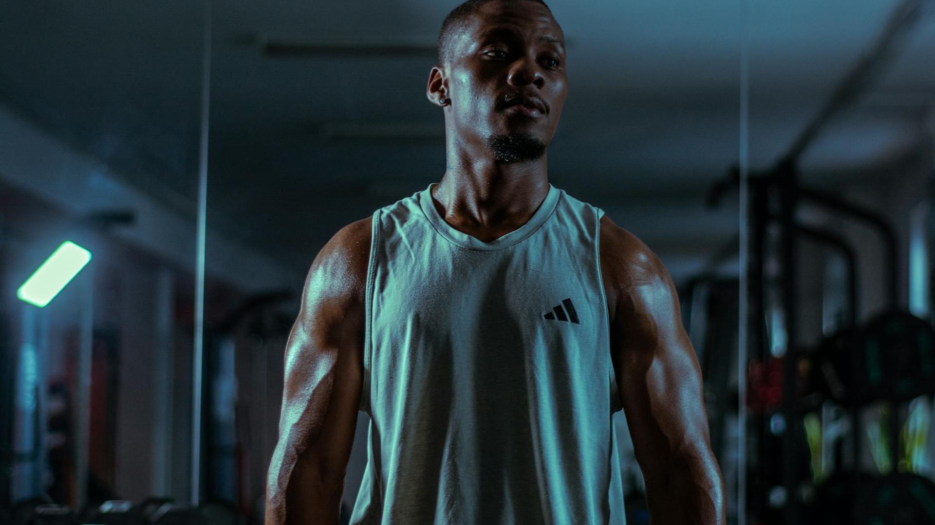 Man in a focused athletic stance in a minimalist dark gym environment.